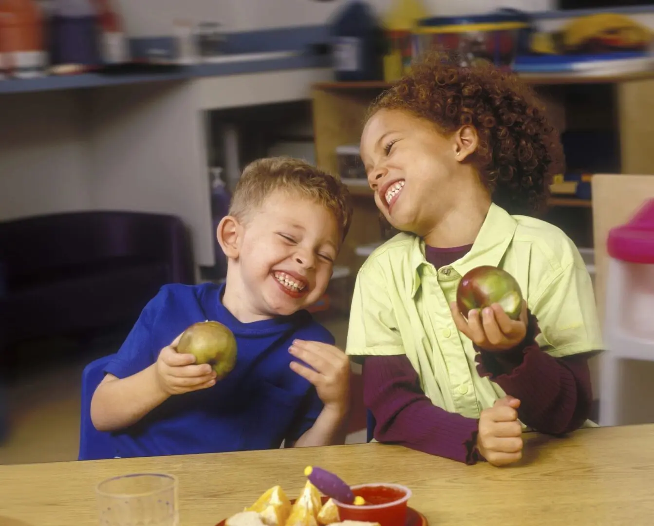 Two children are eating apples at a table.